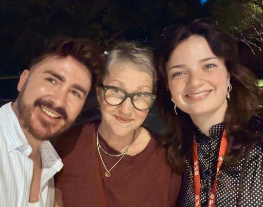 A close-up selfie of me (James), Cathy Wilcox (centre) and Sophie Wishart (right) smiling together at the University of Sydney’s Student Journalism Conference. I’m wearing a light blue striped shirt, Cathy wears black-framed glasses and a burgundy top, and Sophie wears a black polka-dot blouse with a red conference lanyard.