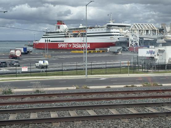 Red and white ship beyond railway tracks.